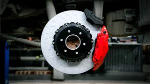 Brake system for Lexus LX600 1 | TRO-NIK : High performance tuning of brake systems | TRO-NIK : High performance tuning of brake systems Close-up of a silver brake rotor with a black center hub and a bright red brake caliper in a workshop setting behind the wheel hub.