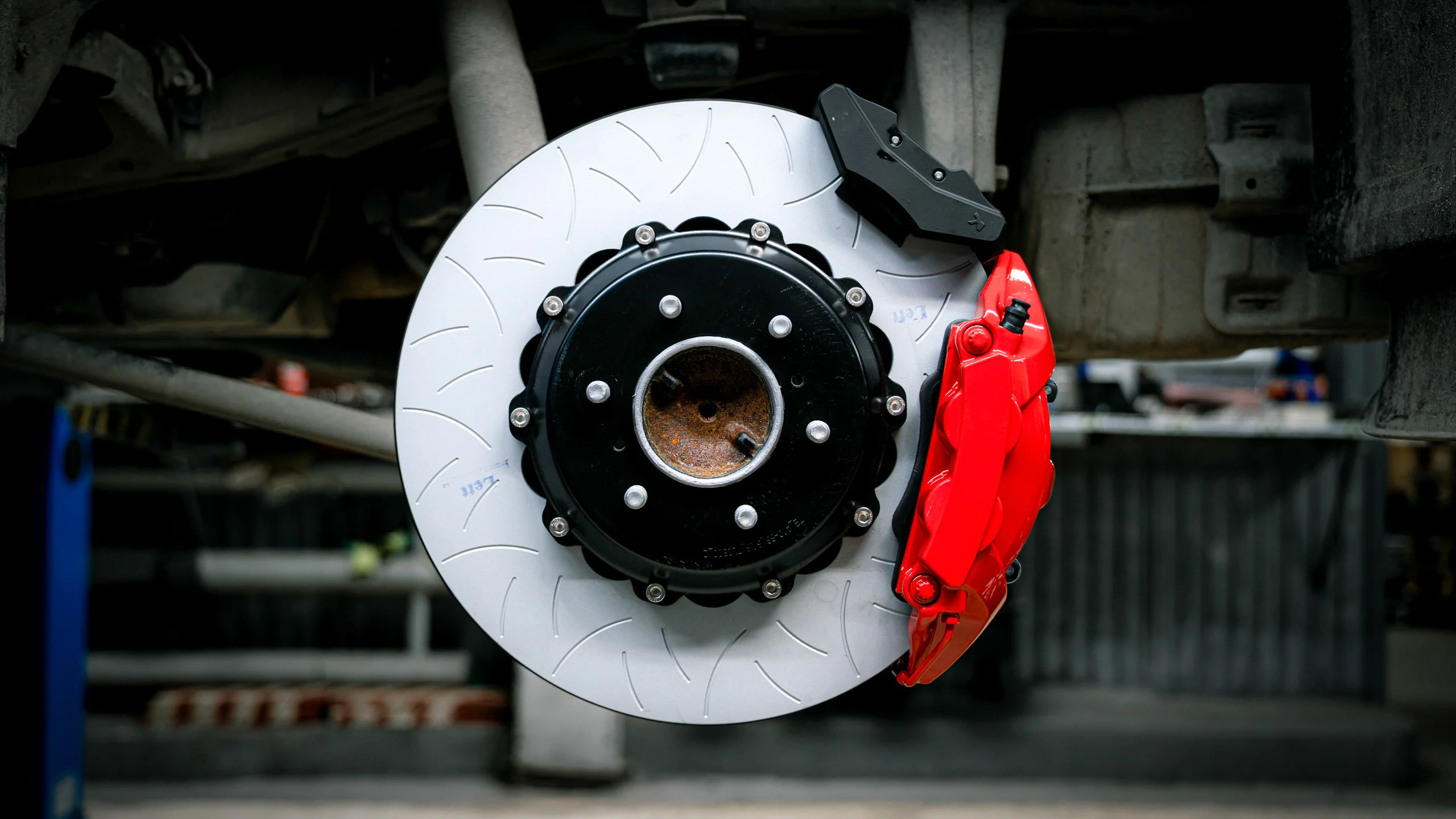 Brake system for Lexus LX600 Picture 1 | Brake system for Lexus LX600 Close-up of a silver brake rotor with a black center hub and a bright red brake caliper in a workshop setting behind the wheel hub.