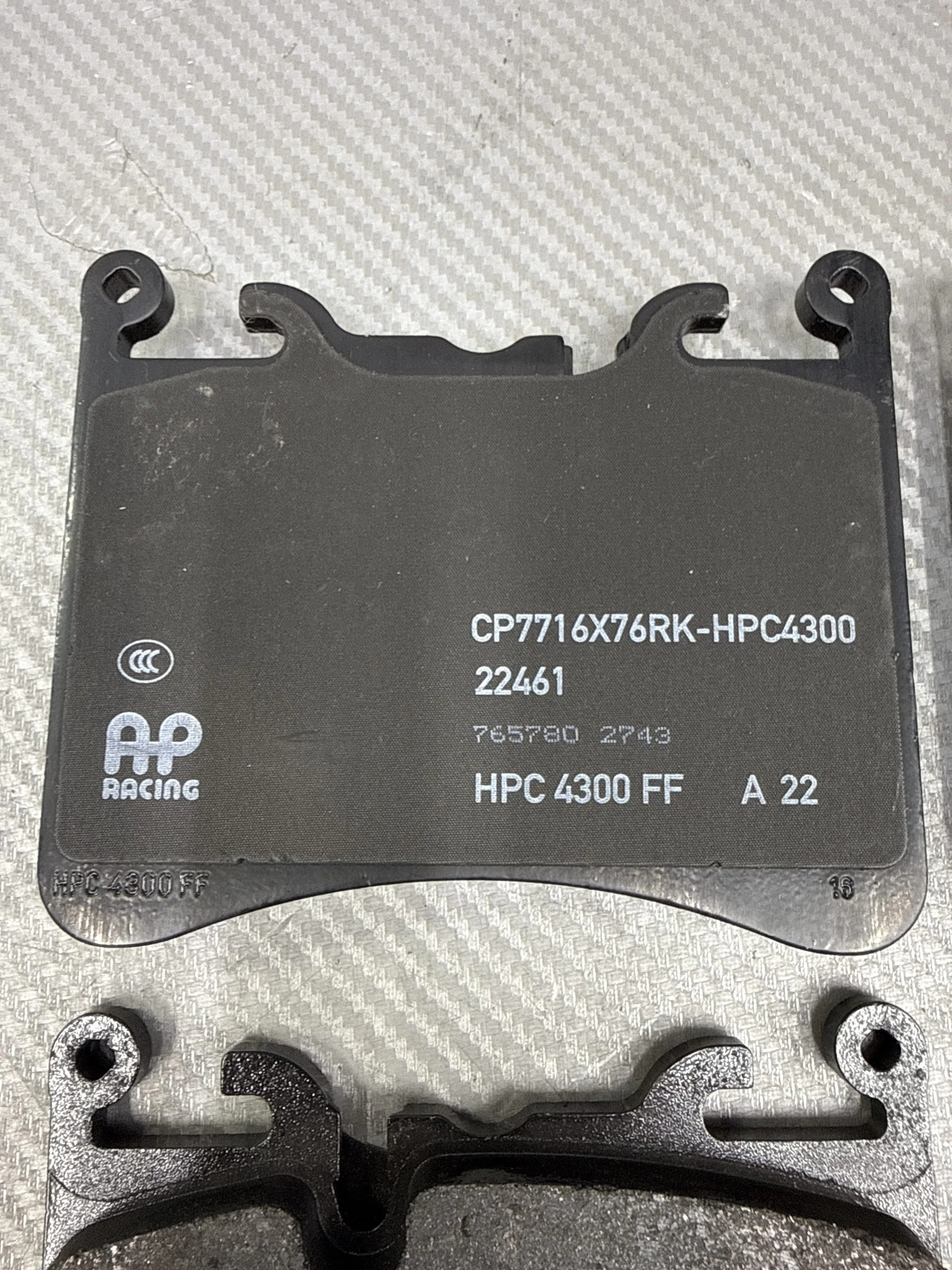 Curved brake pad backing plate with mounting hooks and visible part numbers CP7716X76RK-HPC4300 and HPC4300 FF (AP Racing).
