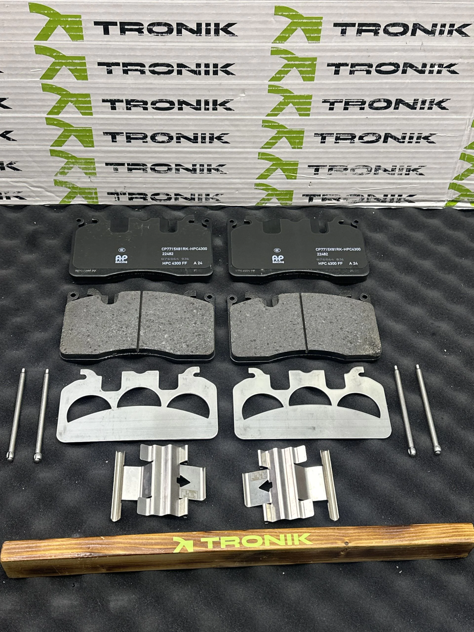 Two pairs of metal brake pads with associated hardware laid out on a TRONIK-branded backdrop.