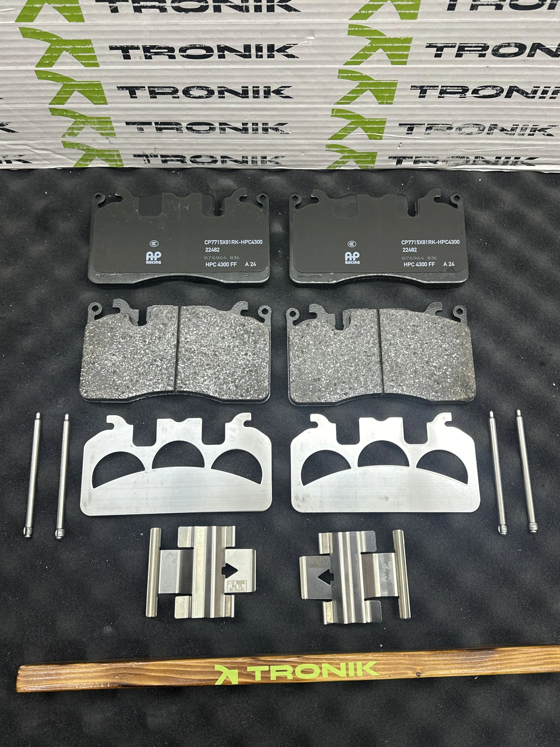 Front brake pads with associated hardware arranged on a black surface; TRONIK packaging visible in the background.