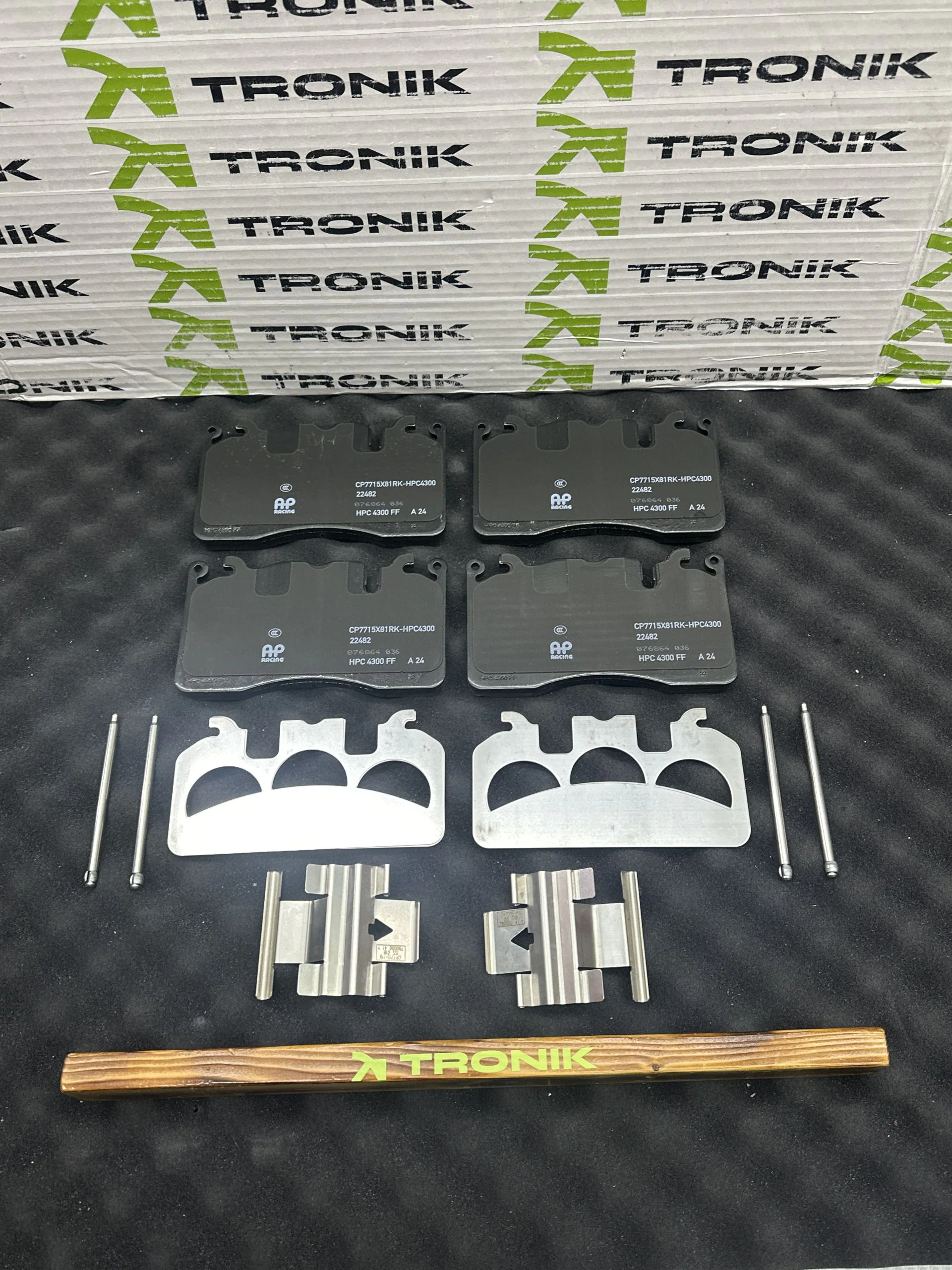 Boxed Tronik brake pads kit with rubberized foam spacers and metal hardware laid out on a black surface