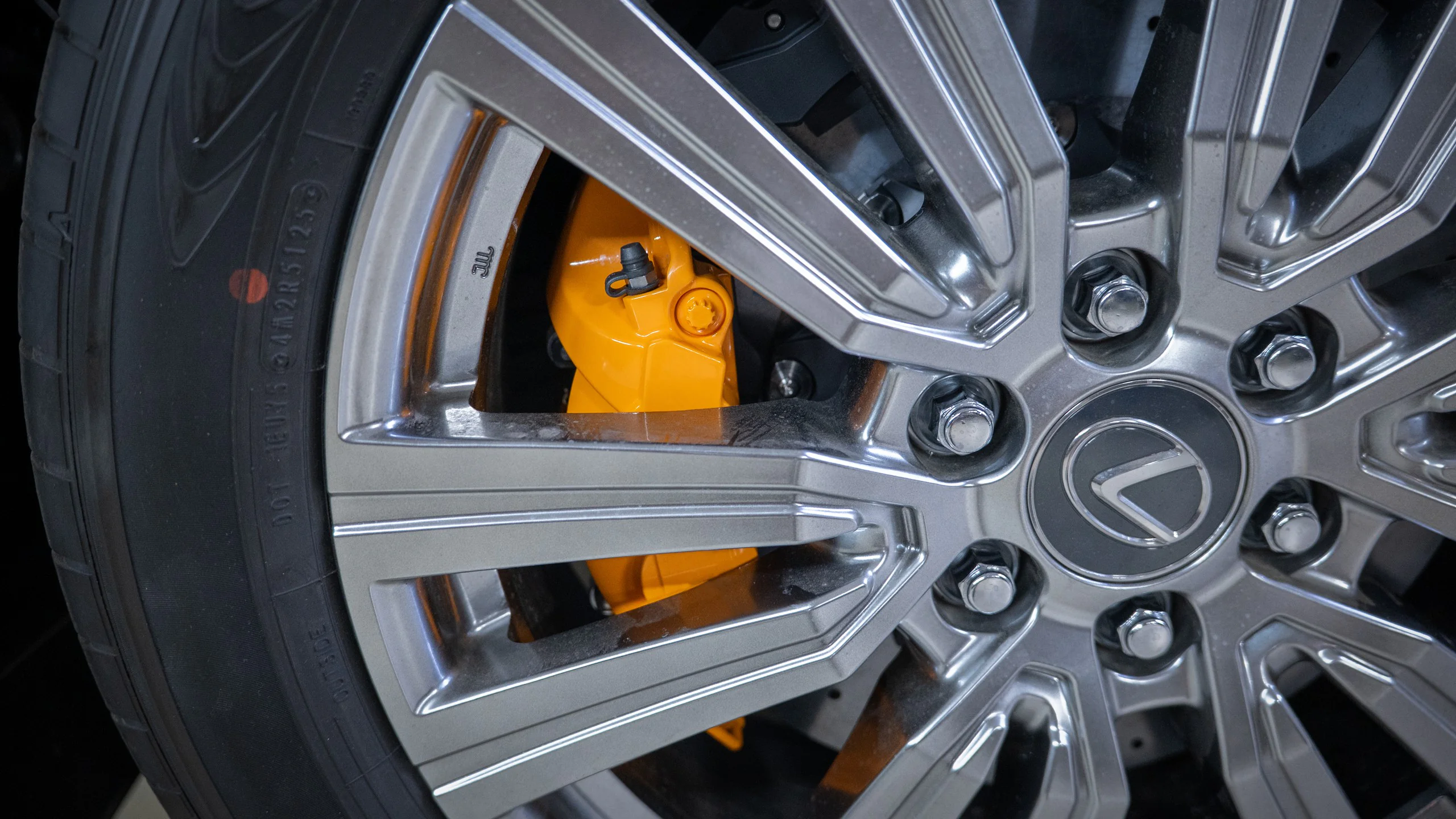 Close-up of a car wheel: silver multi-spoke alloy rim with an orange brake caliper visible through the spokes.
