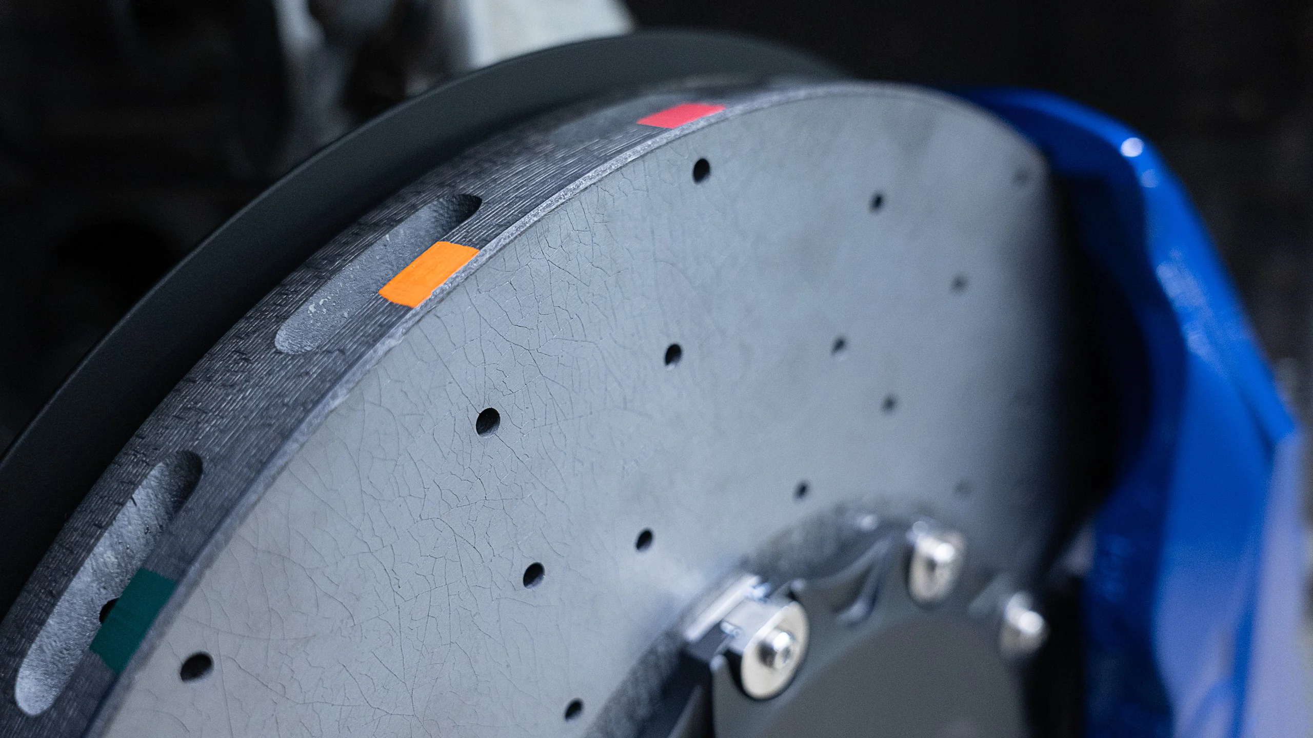 Carbon-ceramic brake system for BMW G07 5 | Carbon-ceramic brake system for BMW G07 | High Performance Tuning of brake systems for all cars: BMW, Mercedes, Audi, VW, Bentley, Maseratti and etc Close-up of a gray metal circular plate with small holes and orange and green markers, blue equipment visible in the background.