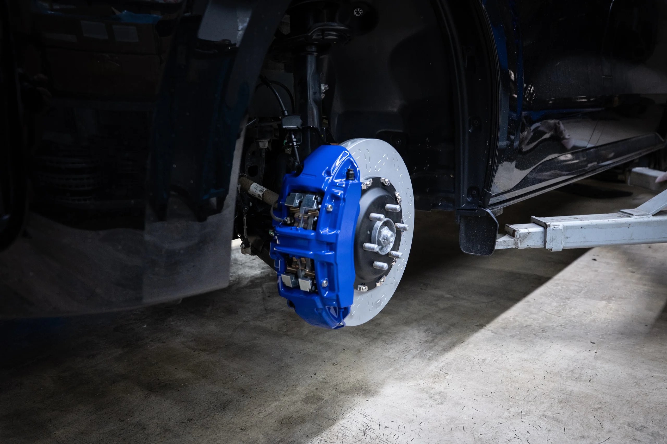 Vehicle with front wheel removed, blue brake caliper and exposed rotor on a car lifted in a garage.