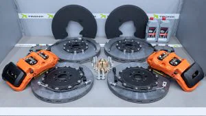 Carbon-ceramic brake system for Zeekr 9X 1 | TRO-NIK : High performance tuning of brake systems | TRO-NIK : High performance tuning of brake systems Two large brake rotors with orange high-performance calipers mounted in a TRONIK testing rig, with branding in the background, and lubricant bottles to the side.