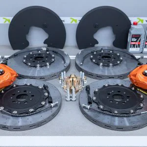 Two large brake rotors with orange high-performance calipers mounted in a TRONIK testing rig, with branding in the background, and lubricant bottles to the side.