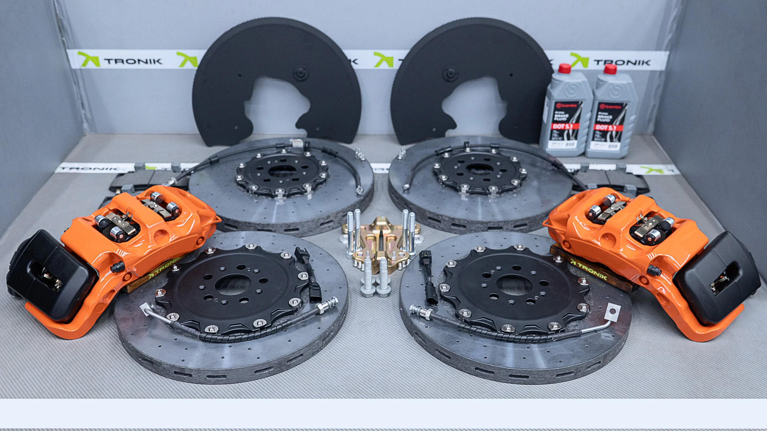 Carbon-ceramic brake system for Zeekr 9X 1 | Carbon-ceramic brake system for Zeekr 9X | High Performance Tuning of brake systems for all cars: BMW, Mercedes, Audi, VW, Bentley, Maseratti and etc Two large brake rotors with orange high-performance calipers mounted in a TRONIK testing rig, with branding in the background, and lubricant bottles to the side.